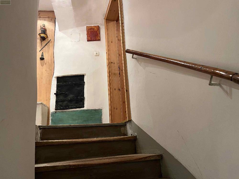 Holztreppe mit Handlauf in einem traditionellen Haus, umgeben von weißen Wänden.