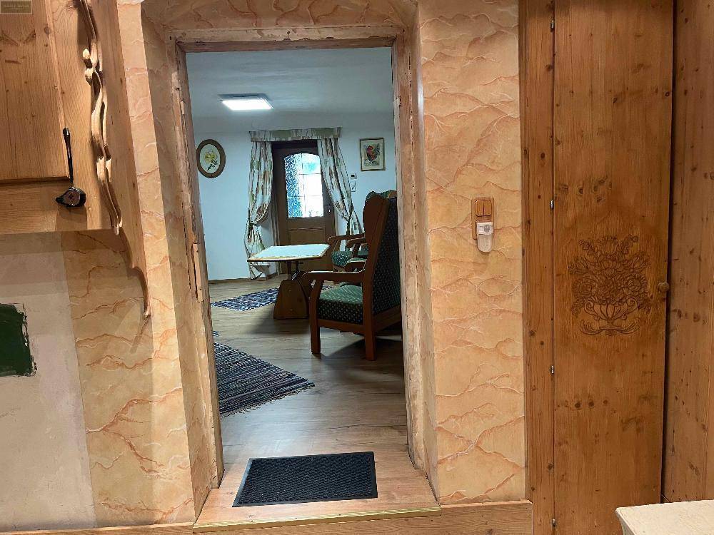 Türöffnung mit Holzverkleidung und dekorativen Elementen, die in ein Wohnzimmer mit Holzboden führt.