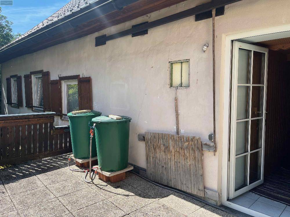 Außenterrasse mit Fliesenboden, zwei grünen Regentonnen und einer Tür, die ins Haus führt.