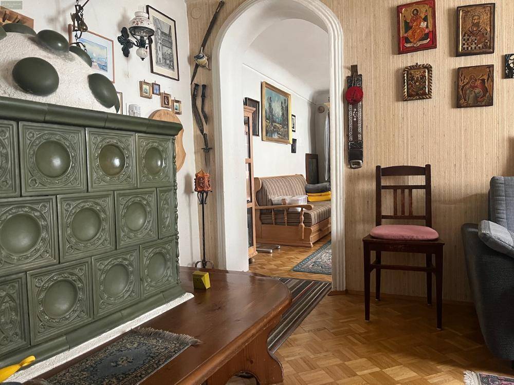 Traditionelles Wohnzimmer mit grünem Kachelofen, Holzmöbeln und Parkettboden, durch einen Bogen verbunden.
