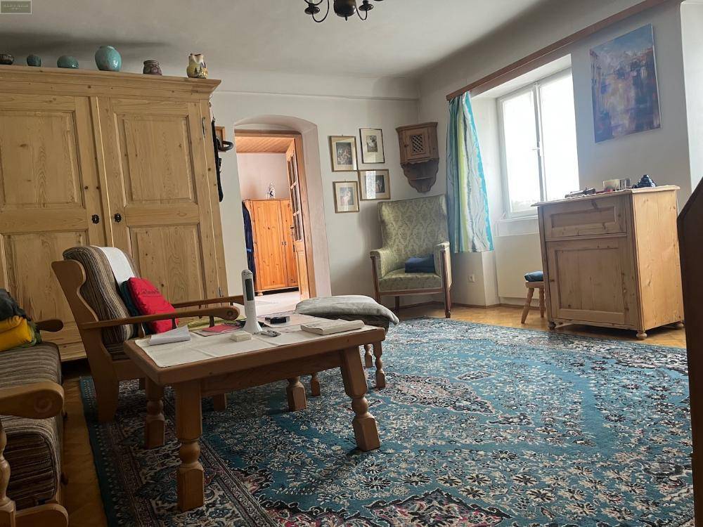Geräumiges Wohnzimmer mit großem Holzschrank, Couchtisch und Sessel, ein blauer Teppich bedeckt den Boden.