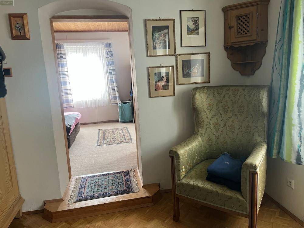Flur oder Übergangsbereich mit Sessel, der in ein Schlafzimmer mit Teppichboden und Fenster führt.