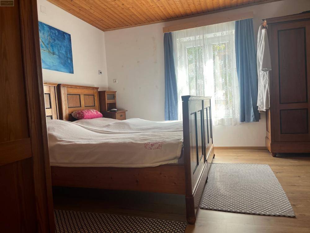 Schlafzimmer mit großem Holzbett, Holzschrank und Fenster mit blauen Vorhängen, Holzboden und Holzdecke.