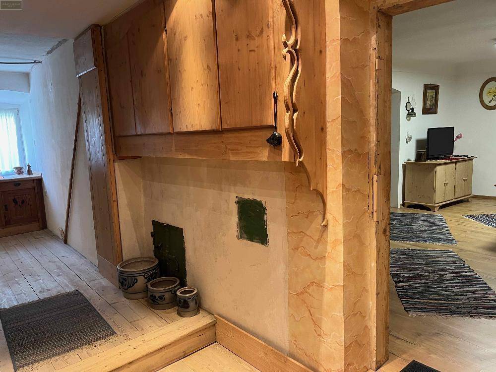 Innenraum mit Holzverkleidung und eingebauter Struktur, möglicherweise ein traditioneller Ofen, führt in einen anderen Raum.