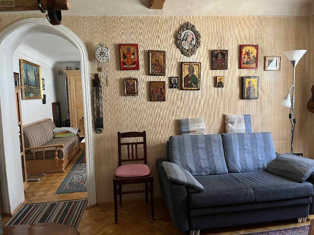Wohnzimmer mit beigem Sofa, Holzstuhl und Parkettboden, die Wand ist mit religiösen Ikonen geschmückt.