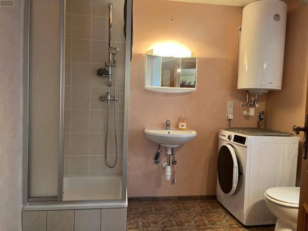 Badezimmer mit Dusche, Waschbecken, Toilette und Waschmaschine, gefliester Boden und hellrosa Wände.