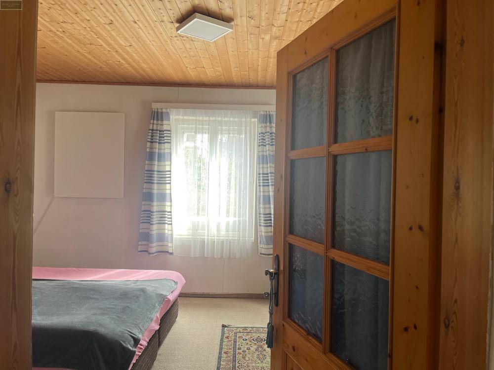 Helles Schlafzimmer mit Holzbalkendecke, Teppichboden und einem Fenster mit gestreiften Vorhängen.