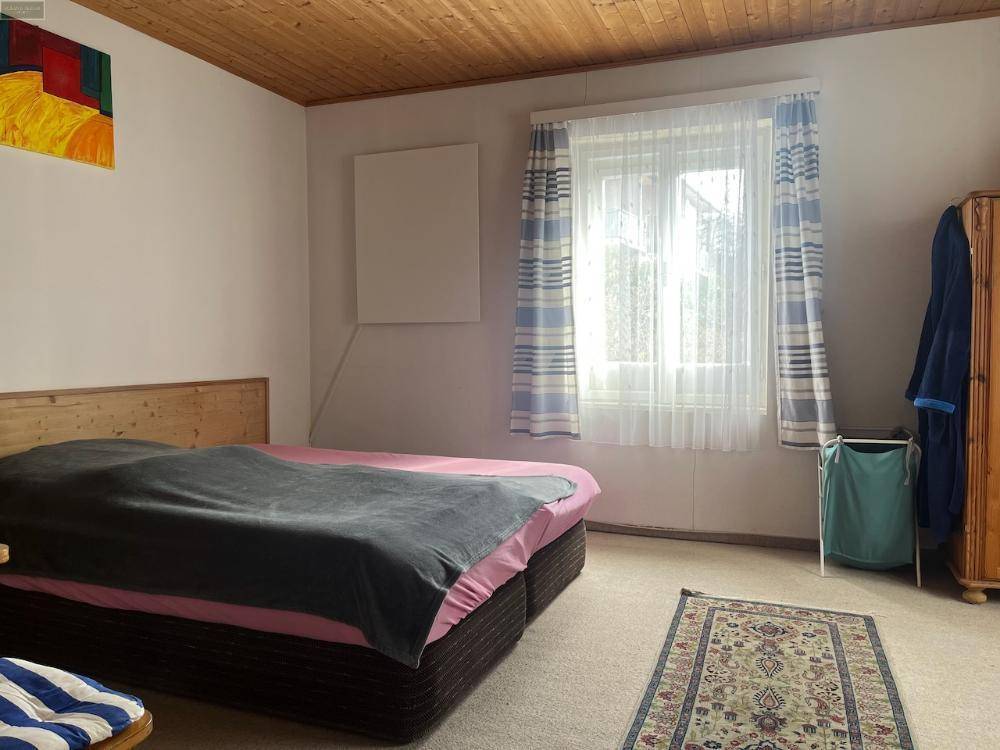 Gemütliches Schlafzimmer mit Holzbalkendecke, Doppelbett und einem Fenster, das viel Tageslicht hereinlässt.