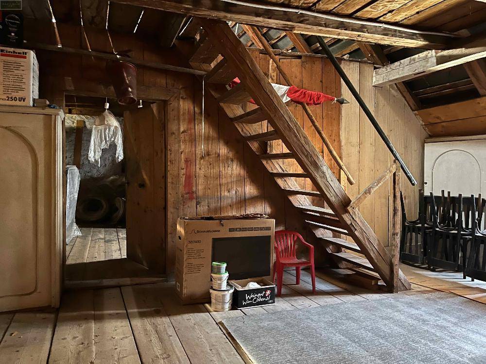 Unausgebauter Dachboden mit sichtbaren Holzbalken und einer Holztreppe, die zu weiteren Ebenen führt.