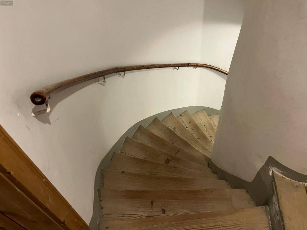 Wendeltreppe aus Holz mit einem geschwungenen Handlauf und weißen Wänden.