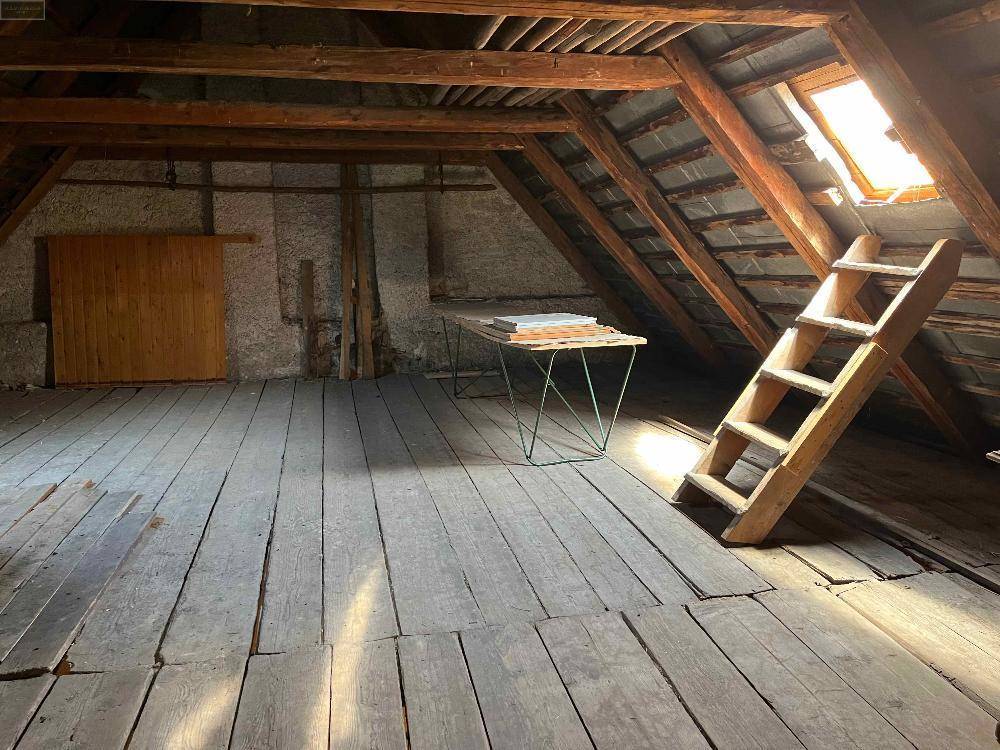 Großer Dachbodenraum mit alten Holzfußböden, sichtbaren Balken und einem Dachfenster mit Leiter.