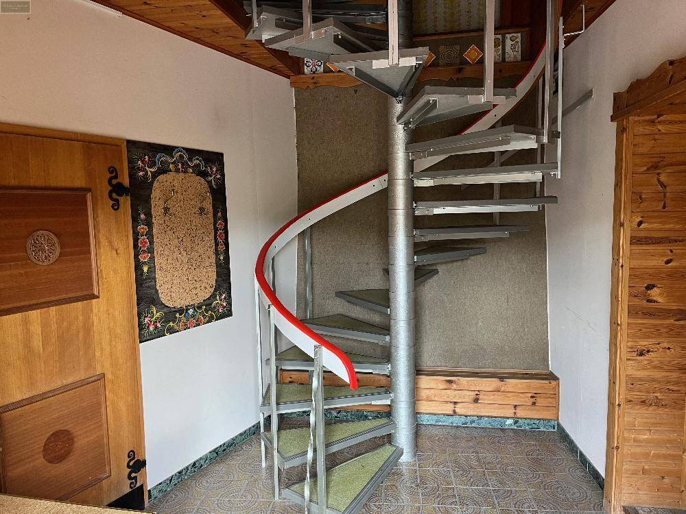 Moderne Wendeltreppe mit Metallstufen und rotem Handlauf in einem holzvertäfelten Eingangsbereich.