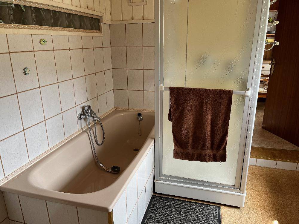 Badezimmer mit Badewanne und Duschkabine, ausgestattet mit hellen Wandfliesen.