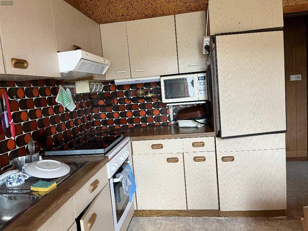 Küche mit beigen Schränken, Mikrowelle und einem auffälligen Fliesenmuster an der Wand.