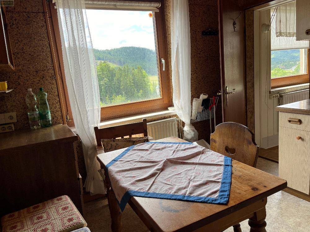 Helle Essküche mit Holztisch und Fenster, das einen weiten Blick ins Grüne bietet.