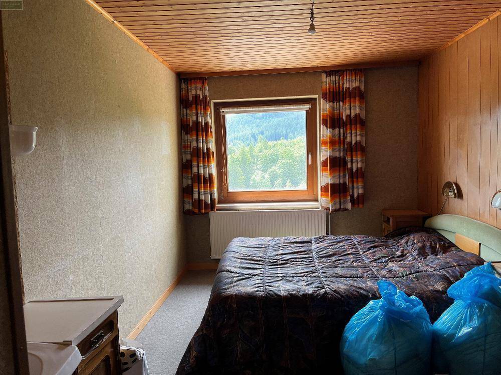 Schlafzimmer mit Doppelbett, gemusterten Vorhängen und Fensterblick auf die Natur.