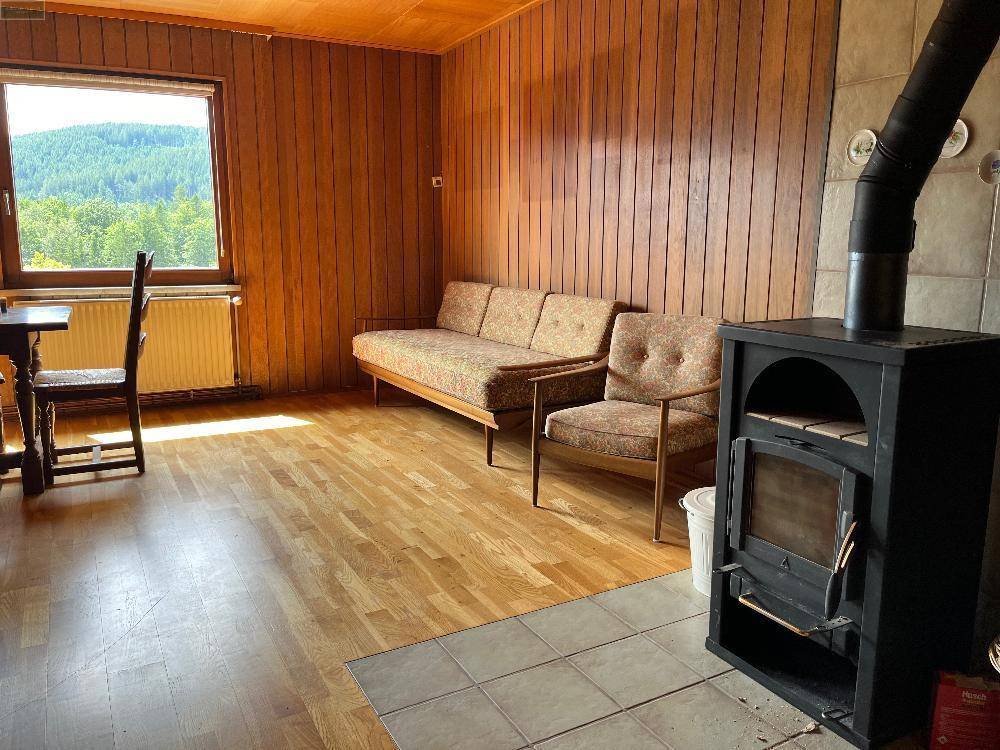 Gemütliches Wohnzimmer mit Holzvertäfelung, Sitzmöbeln und einem Kaminofen.