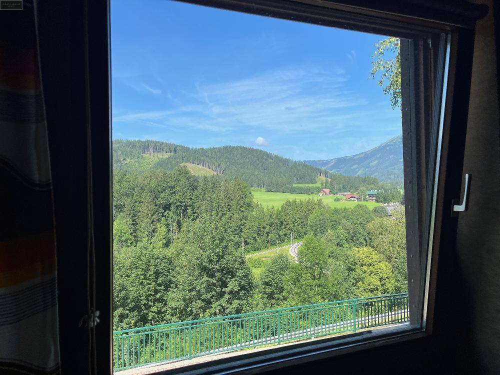 Detailansicht aus einem Fenster mit weitem Blick über eine grüne Landschaft und Berge.