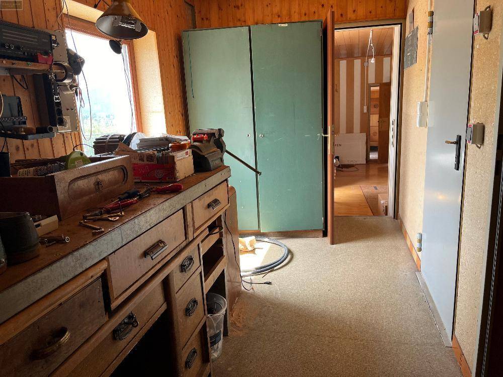 Werkstattbereich mit Holzwerkbank, verschiedenen Werkzeugen und Blick in einen angrenzenden Flur.