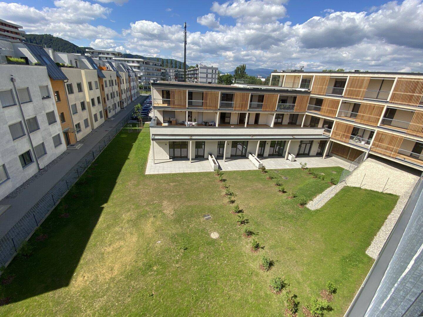 Vogelperspektive des Wohnkomplexes mit seinen Grünflächen und der umliegenden Bebauung unter blauem Himmel.