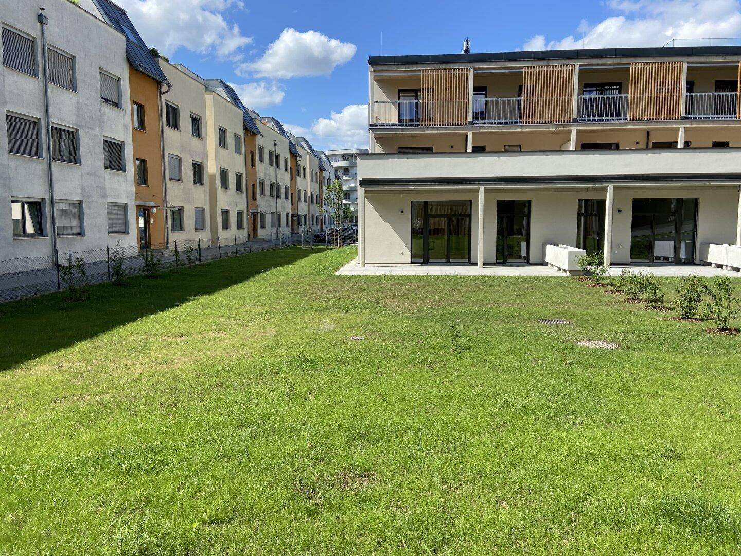 Ansicht des modernen Wohnkomplexes mit seinen Balkonen und der weitläufigen Rasenfläche an einem sonnigen Tag.