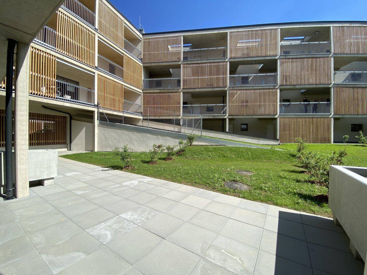 Geräumige Terrasse mit Steinplatten und Blick auf die grüne Gemeinschaftsfläche des modernen Wohnkomplexes.