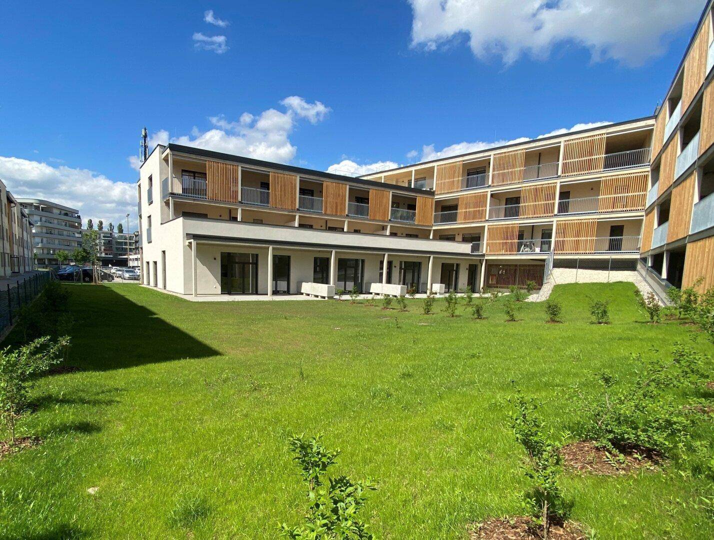 Weitläufige Rasenfläche vor einem modernen Wohngebäude mit Holzverkleidung und Balkonen.