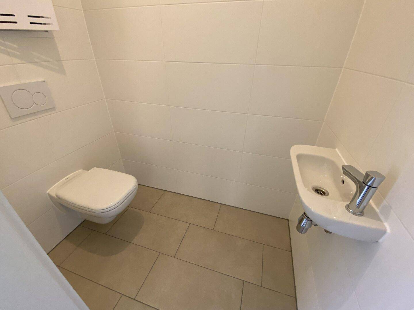 Modernes Gäste-WC mit Wand-WC, kleinem Waschbecken und hellen Fliesen.