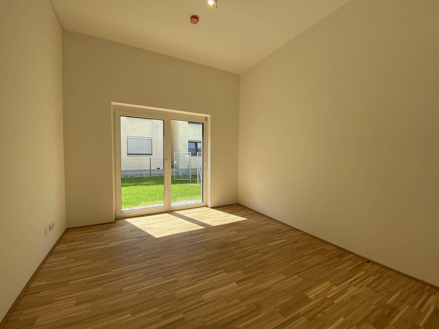 Heller Raum mit Holzparkett und großem Fenster, das viel Sonnenlicht in den Raum bringt.