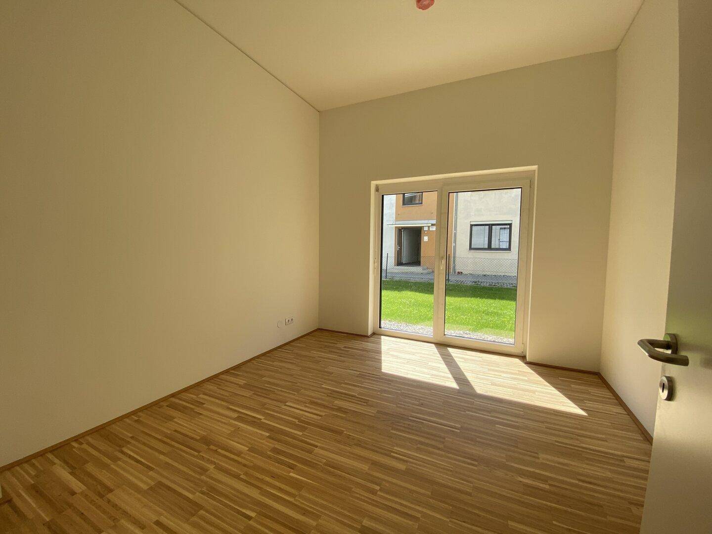 Sonniger Raum mit Holzparkett und Zugang zu einem Außenbereich durch eine Fenstertür.