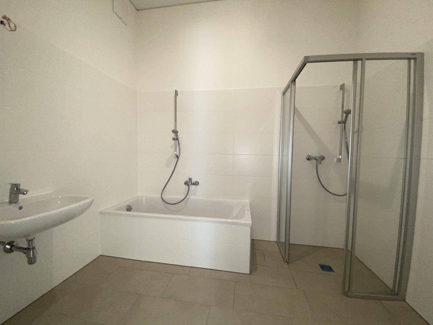 Helles Badezimmer mit Badewanne, Dusche, Waschbecken und beigefarbenen Fliesen.