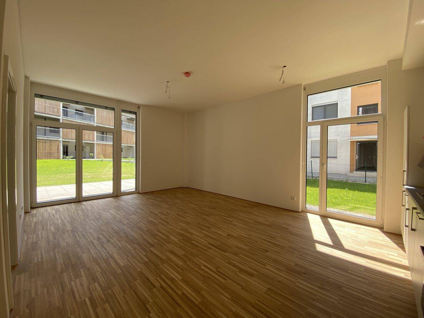Lichtdurchfluteter Wohnraum mit Holzparkett und großen Fenstertüren zum Außenbereich und Garten.