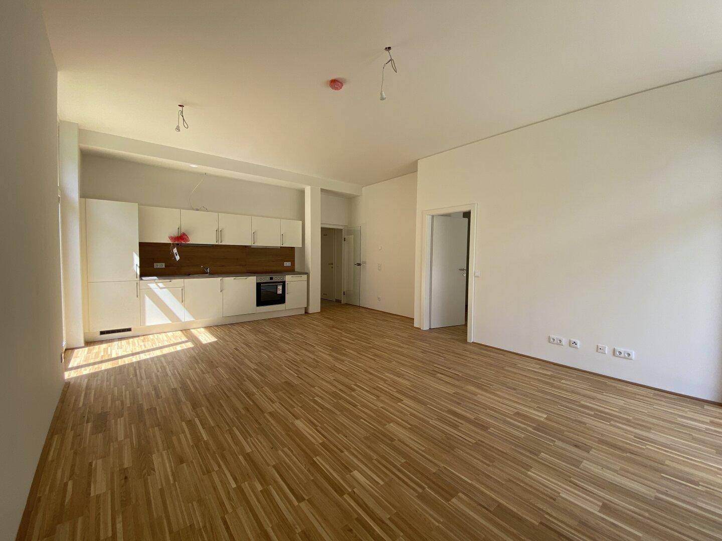 Geräumiger, heller Wohnbereich mit Holzparkett und integrierter Küchenzeile in einem Neubau.