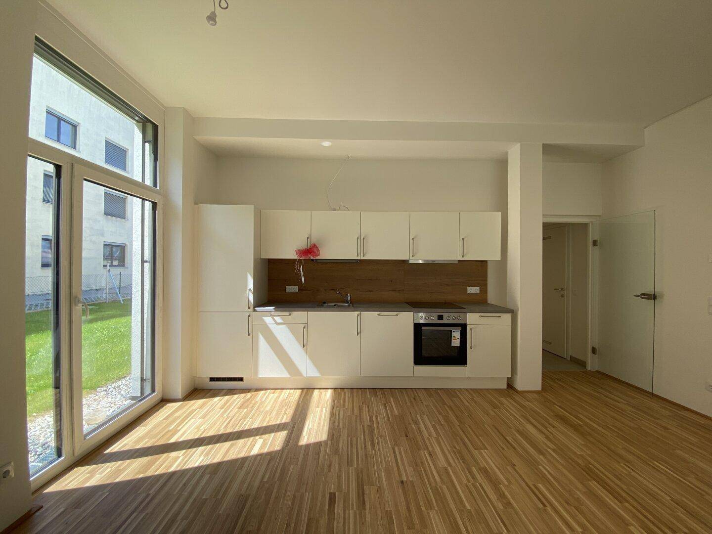Helle, offene Küche mit weißer Einbauküche, Holzparkett und großem Fenster zum Garten.