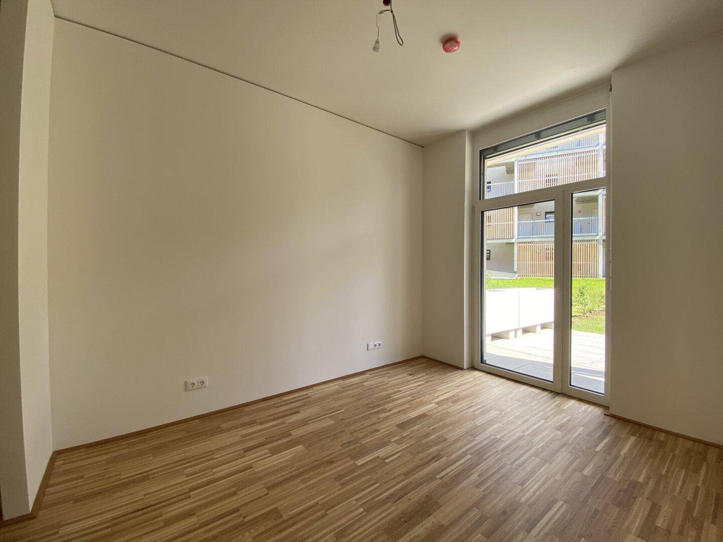 Heller Raum mit Holzparkett und großer Fenstertür, die viel Tageslicht hereinlässt.