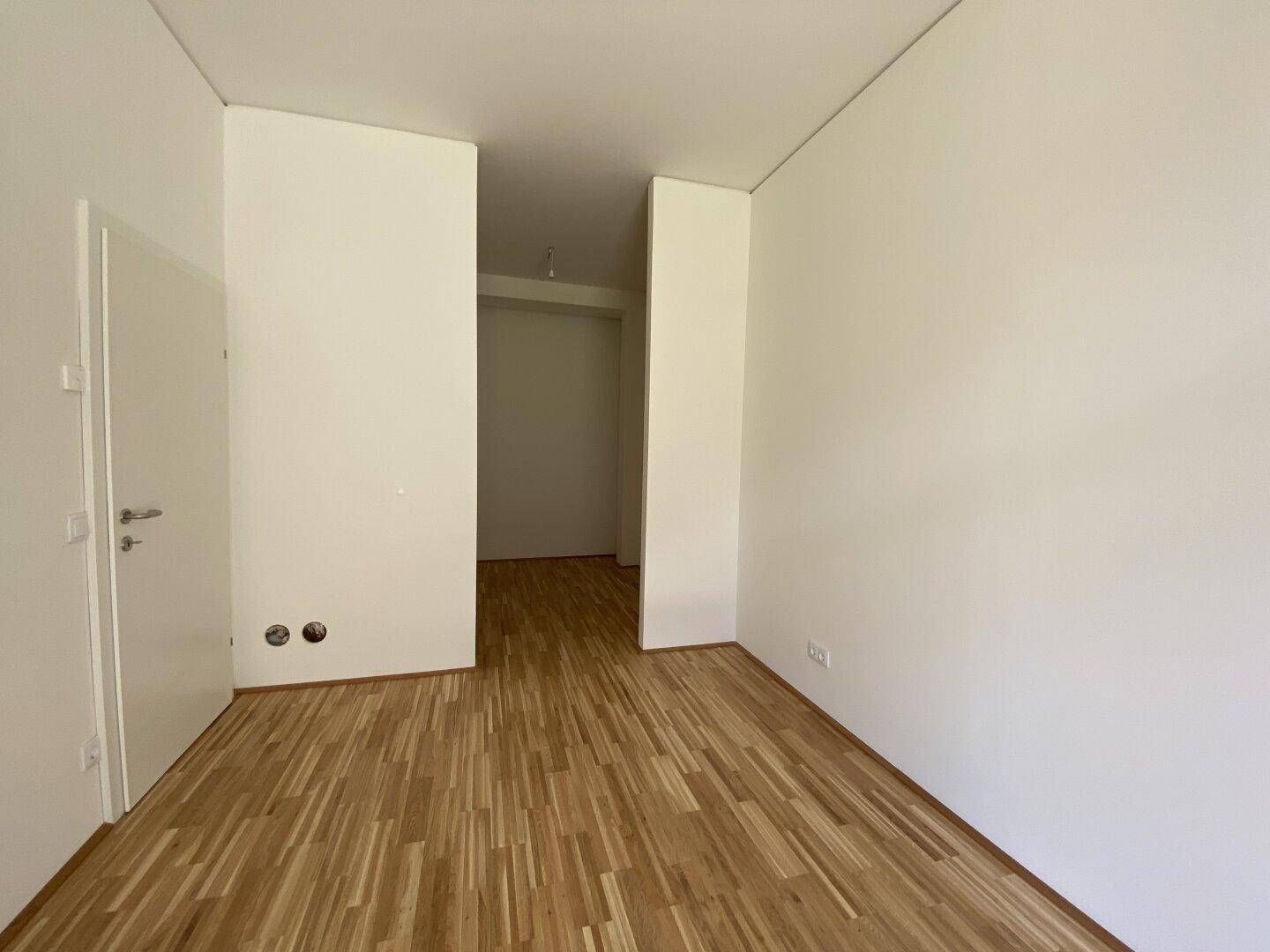 Leerer Raum mit Holzparkett und weißen Wänden, bereit für individuelle Gestaltung und Nutzung.