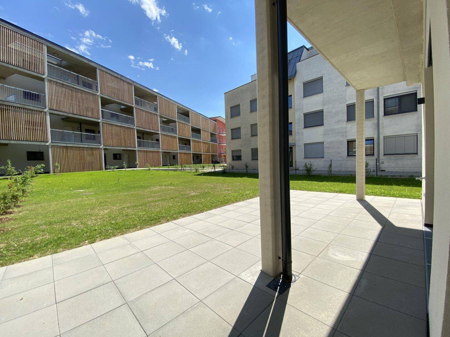 Überdachte Terrasse mit Fliesenboden und Blick auf die umliegenden Neubauwohnungen und Grünflächen.