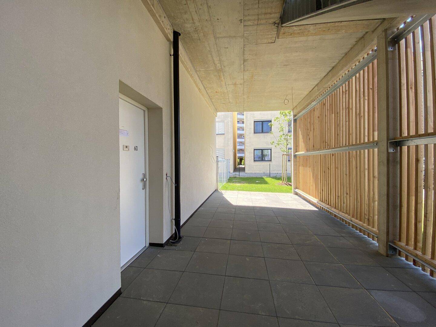 Überdachter Zugangsbereich mit Fliesenboden und Holzverkleidung, der zum Garten führt.