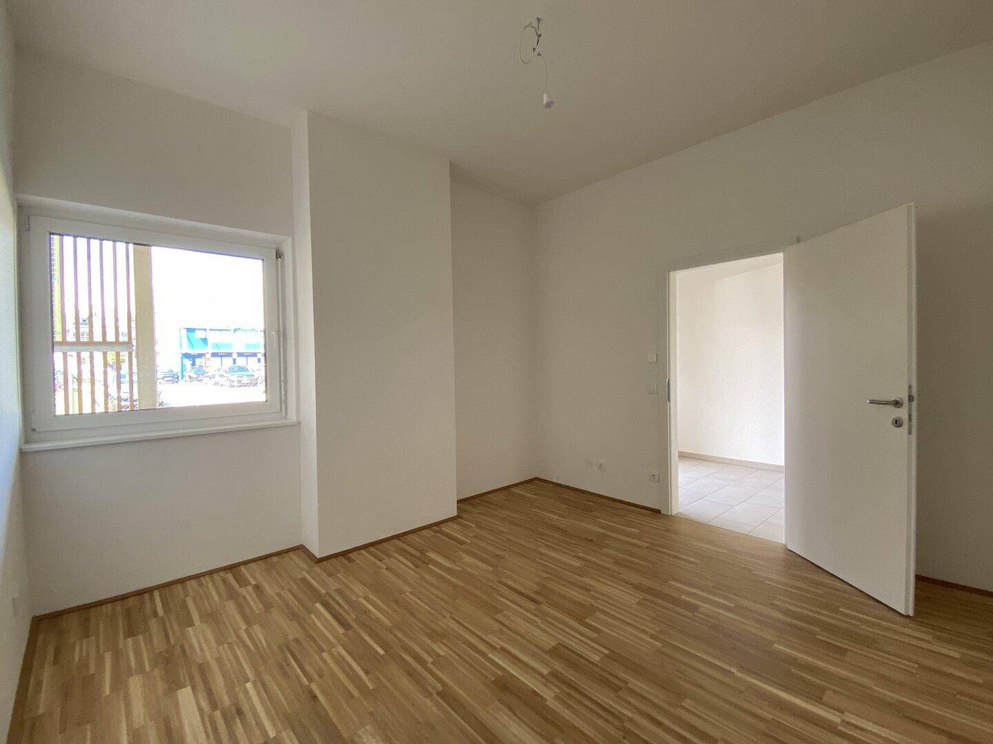 Ruhiges Schlafzimmer mit Parkettboden und einem Fenster, das Tageslicht hereinlässt.