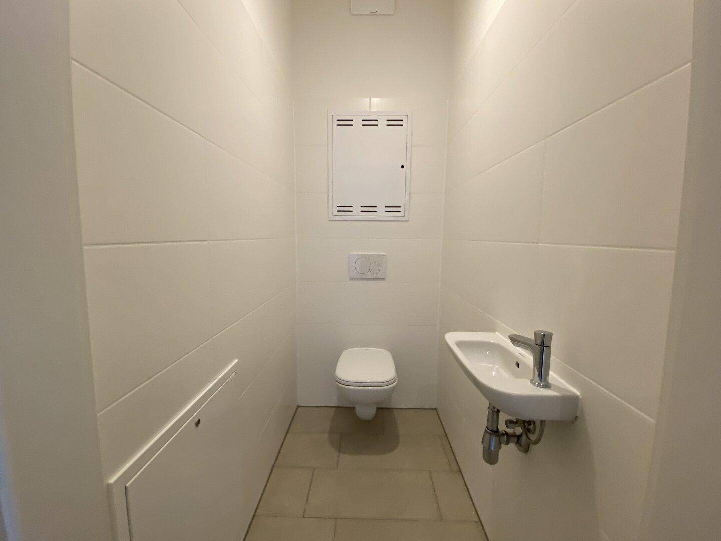 Modernes Gäste-WC mit wandhängender Toilette und kleinem Waschbecken, komplett gefliest.
