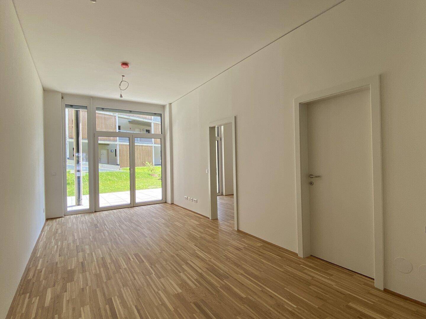 Geräumiger, heller Wohnraum mit Parkettboden und großen Fenstern zum Außenbereich.
