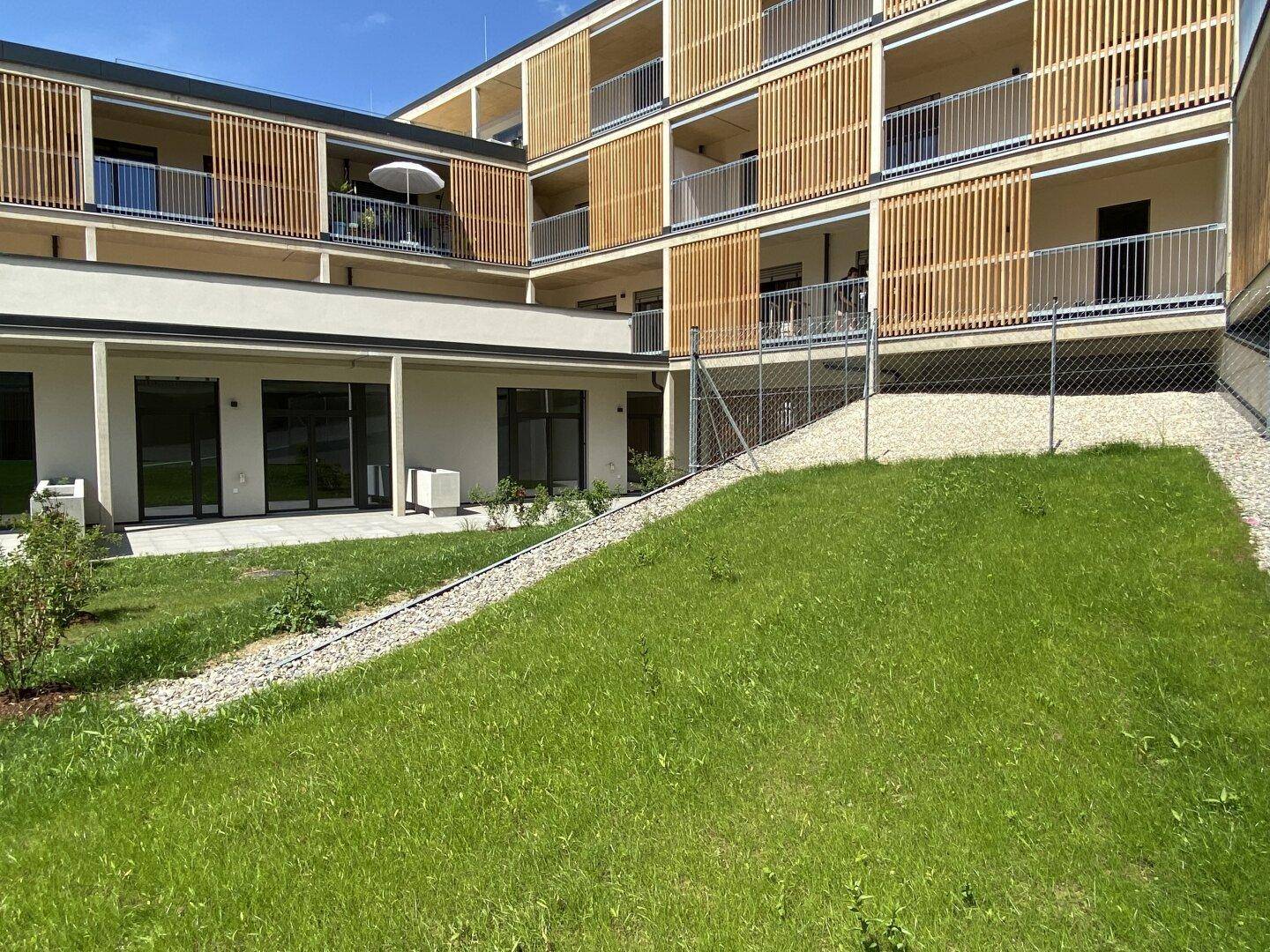 Moderne Wohnanlage mit Holzfassade, Balkonen und einer gepflegten Grünfläche im Vordergrund.