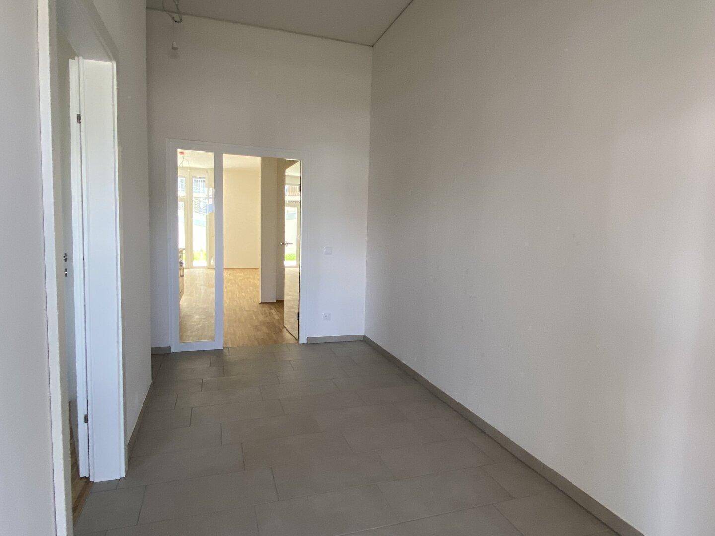 Geräumiger Flur mit Fliesenboden und Blick durch Glastüren in den angrenzenden Wohnbereich.