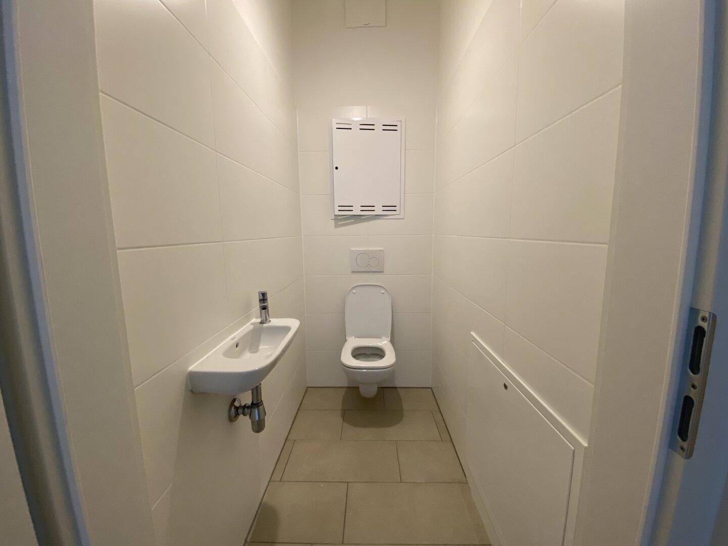 Modernes Gäste-WC mit hellen Fliesen, wandhängendem WC und kleinem Waschbecken.