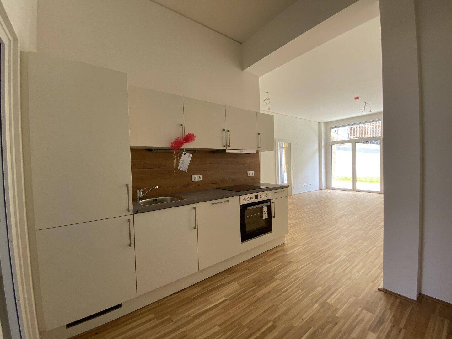 Moderne Einbauküche mit hellen Schränken und Holzakzenten, offen zum Wohnbereich mit Parkettboden.
