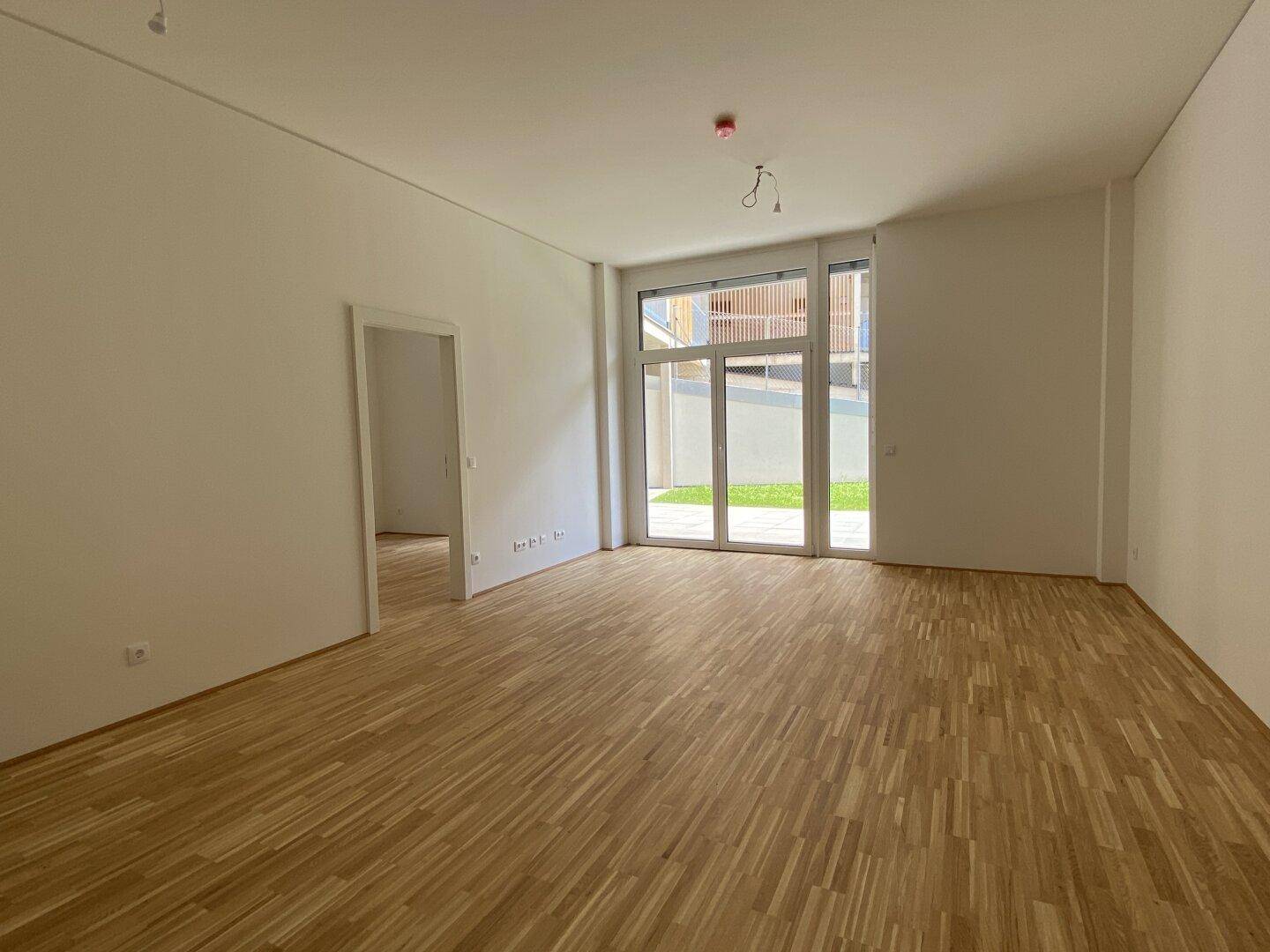 Heller Wohnbereich mit Parkettboden und großen Fenstertüren, die Zugang zum Außenbereich bieten.