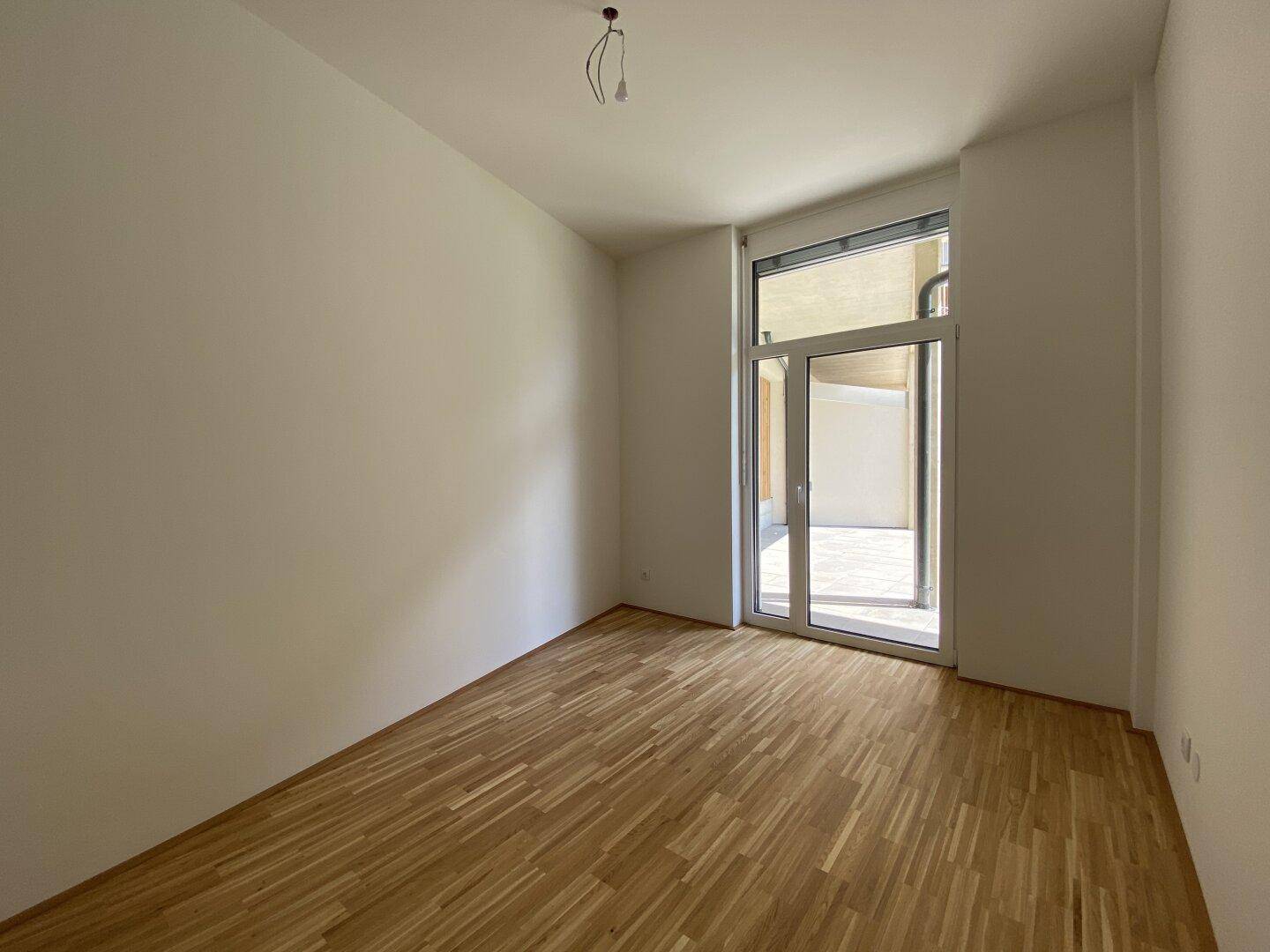 Leerer Raum mit Parkettboden und Zugang zu einem Außenbereich durch eine große Glastür.
