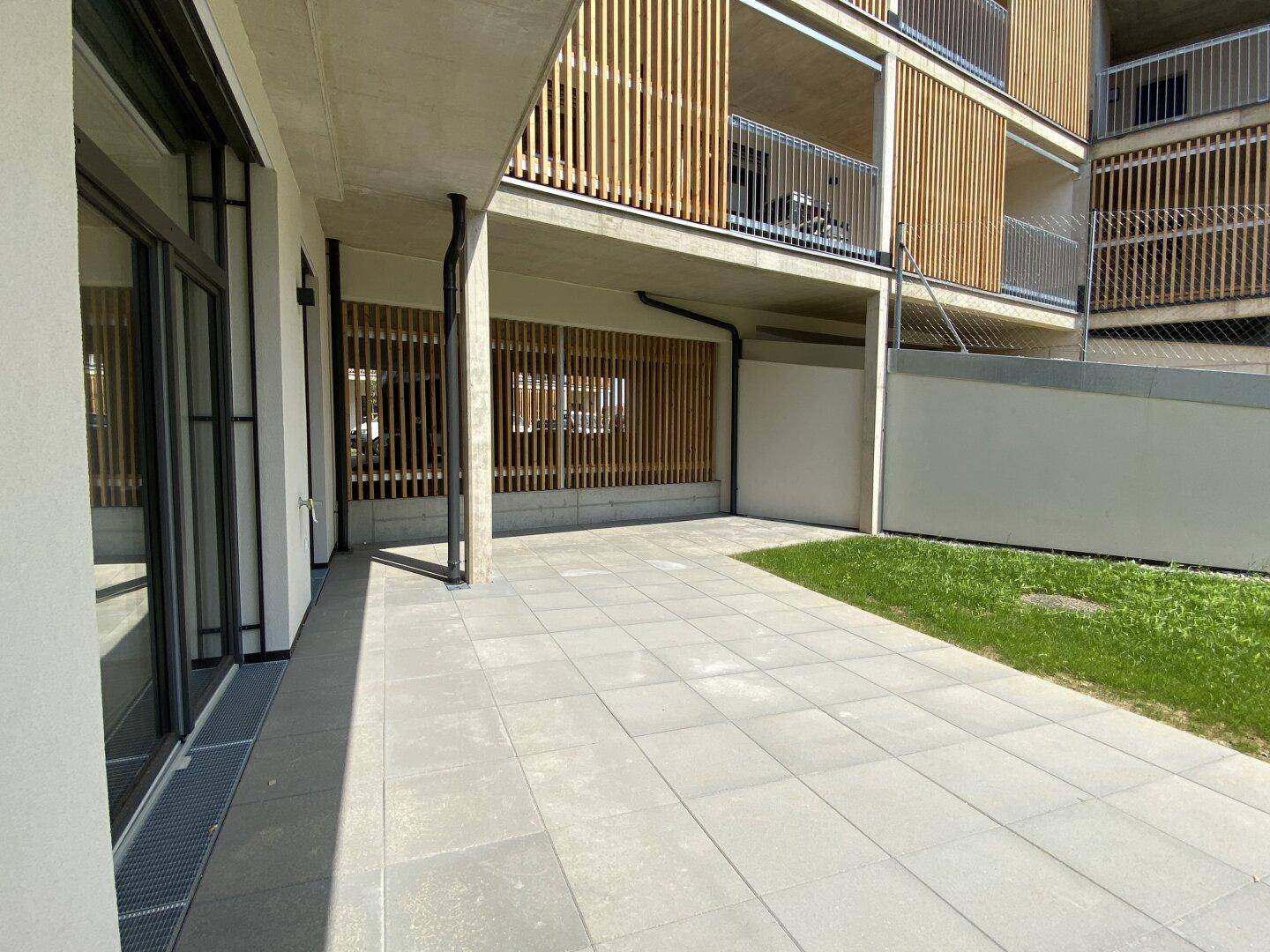 Geräumige gepflasterte Terrasse im Erdgeschoss eines modernen Gebäudes mit Holzelementen.