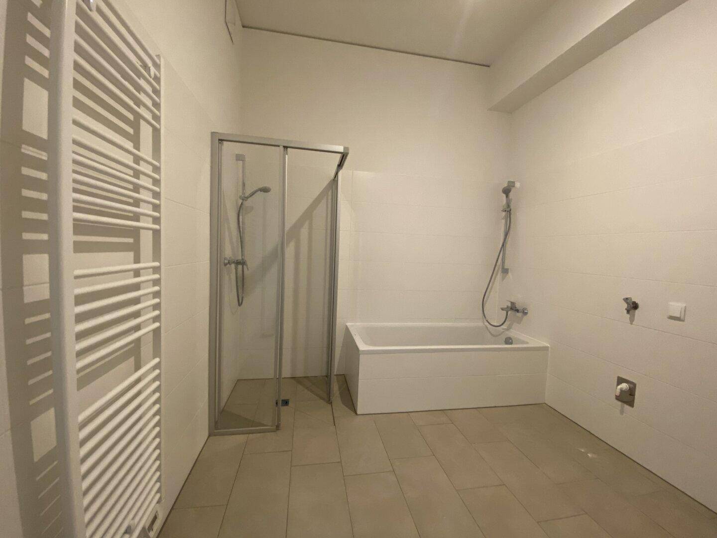 Modernes Badezimmer mit Badewanne, Duschkabine und beheiztem Handtuchhalter.