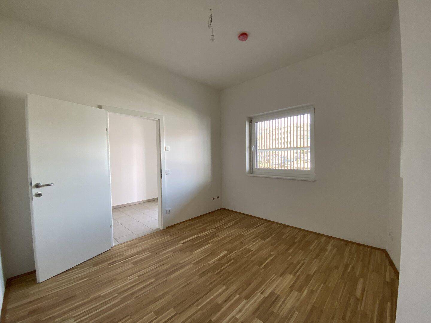 Heller Raum mit Parkettboden und einem Fenster, das für natürliches Licht sorgt.